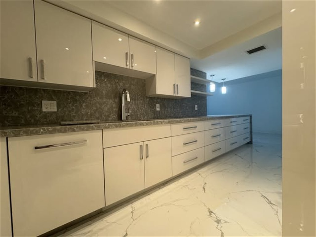Cocina lineal con gabinetes blancos de alto brillo y backsplash de piedra oscura